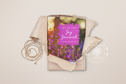 Mockup of A Daydreaming Cactus journal creation. This is the 30 Day Joy Journal with a lavender flowers cover wrapped in wrapping paper as a gift.